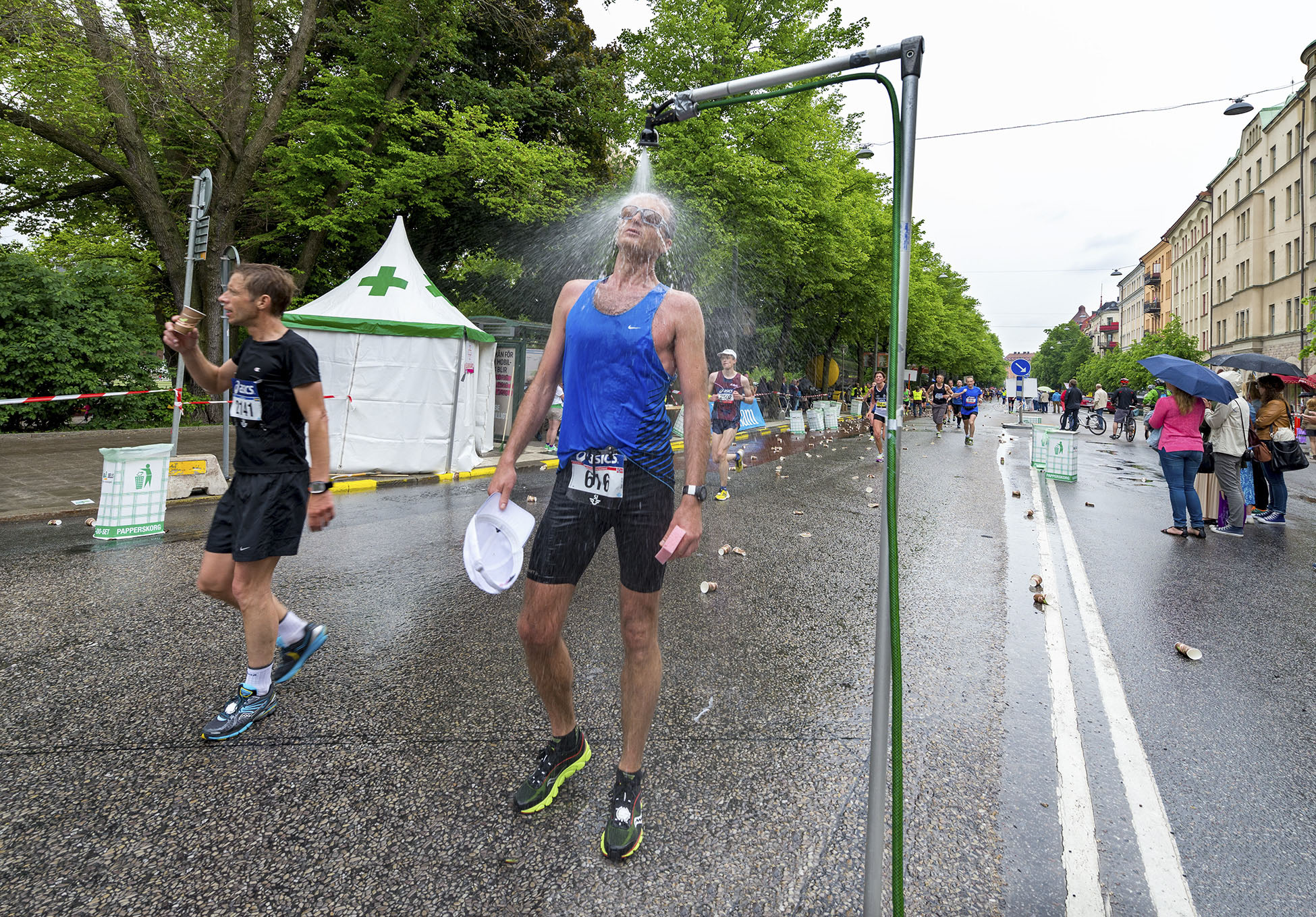 Stockholm Marathon. Löpare svalkar sig under en vattenspridare